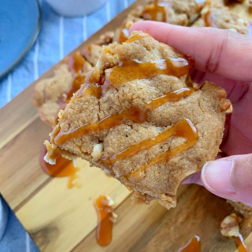 hands holding a slice of brown sugar blondies with caramel drizzle