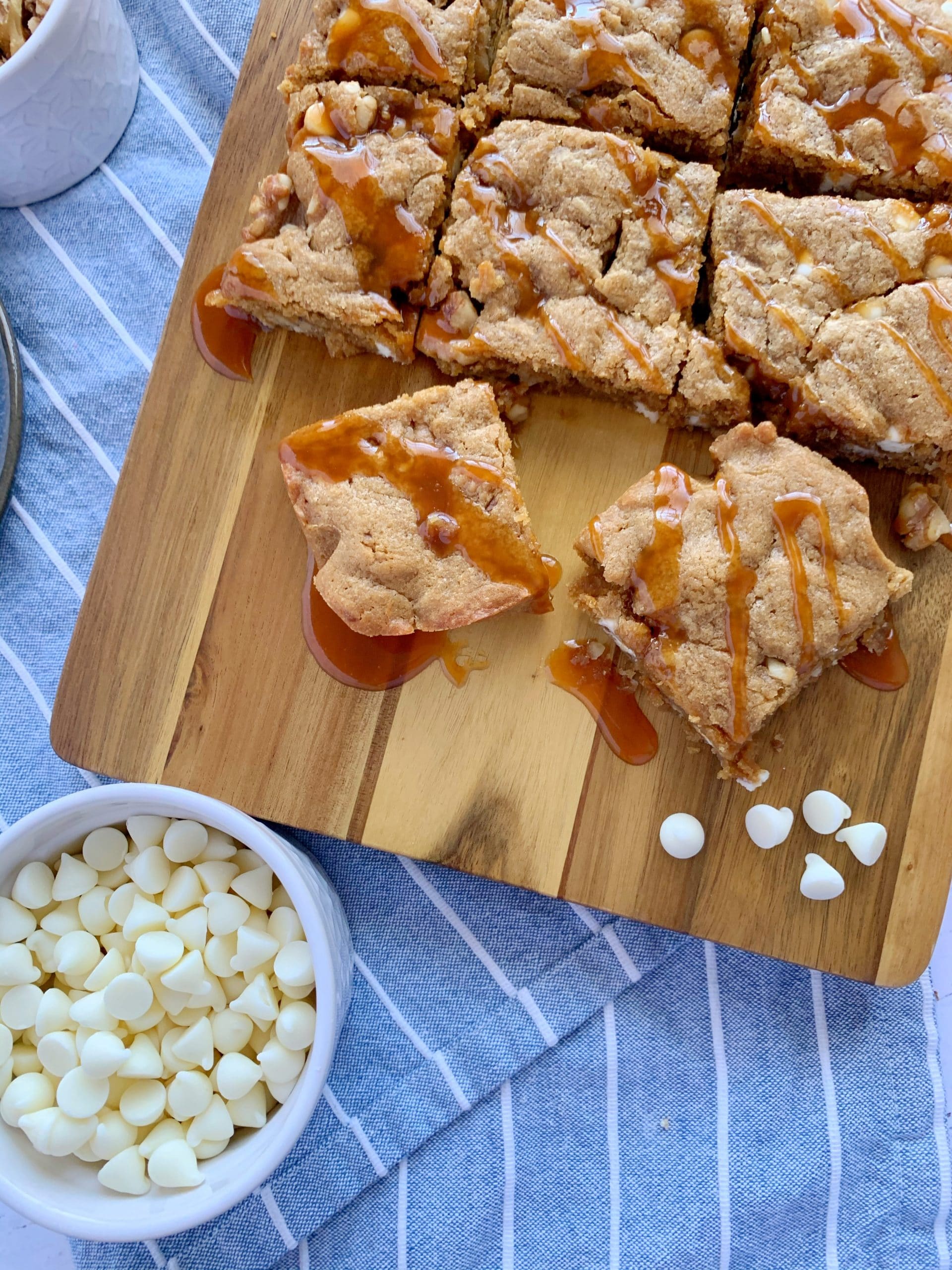 blondies drizzled with caramel on a wooden board with white chocolate chips