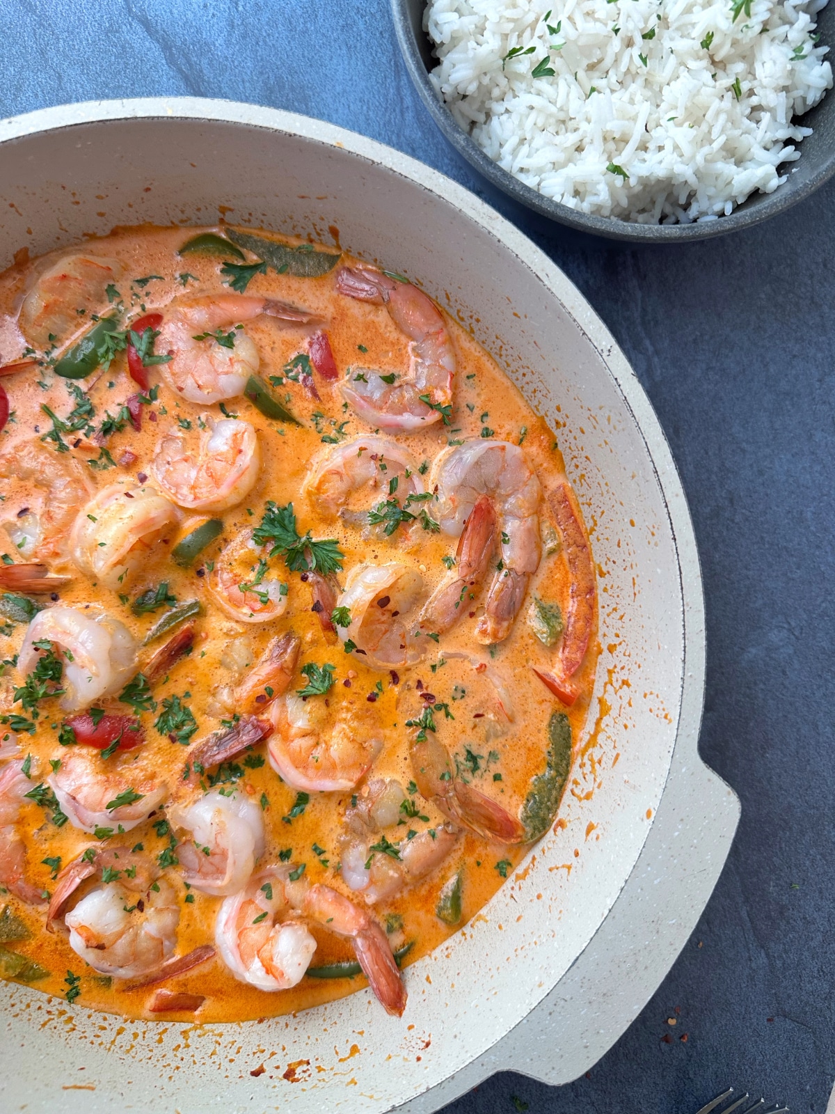 A pan of red shrimp curry alongside a bowl of white rice.