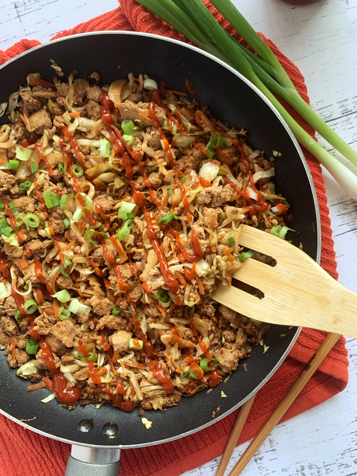 A skillet containing egg roll in a bowl, with a wooden spoon scooping a portion out.