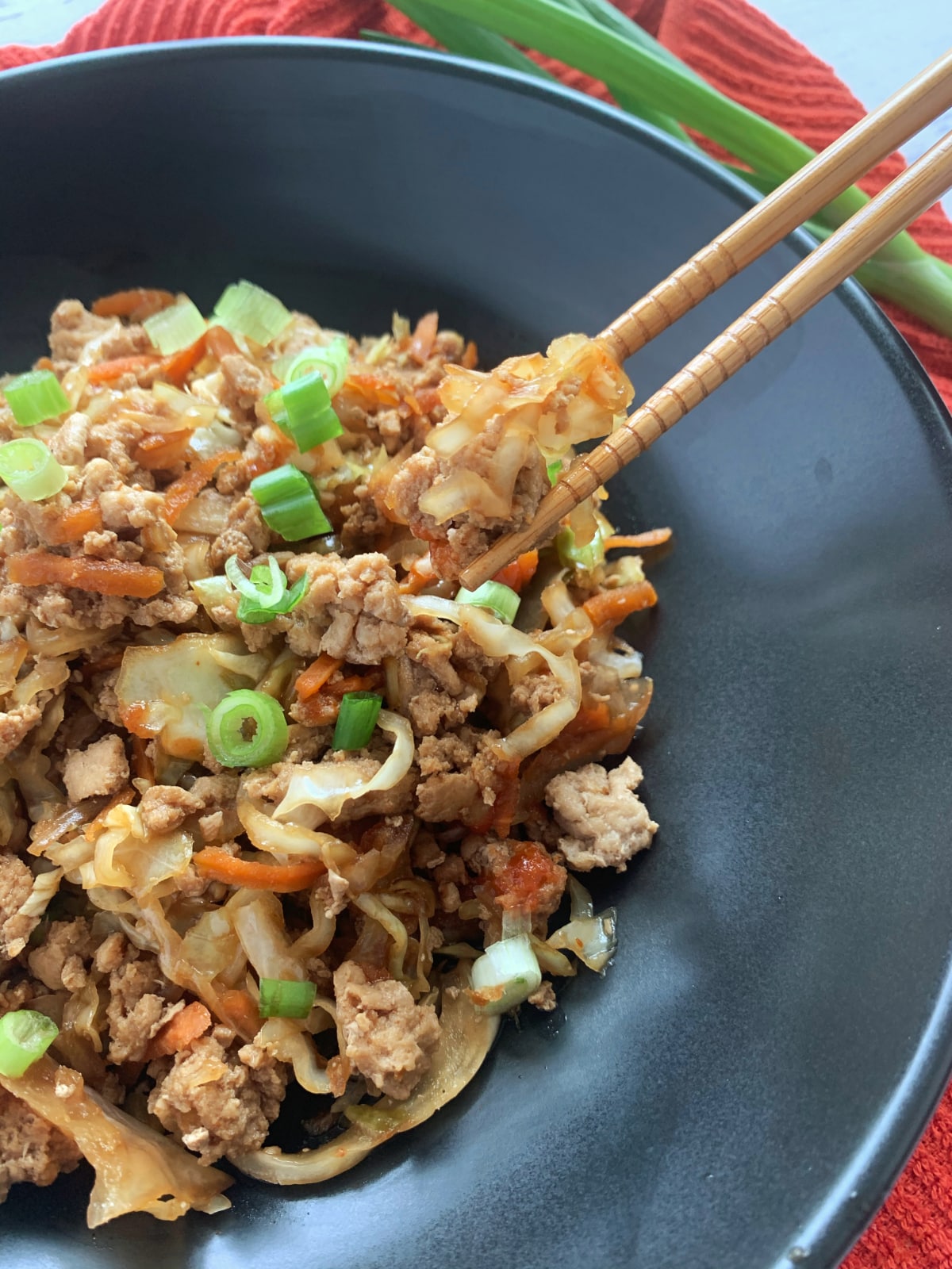 Chopsticks picking up a portion of egg roll in a bowl.