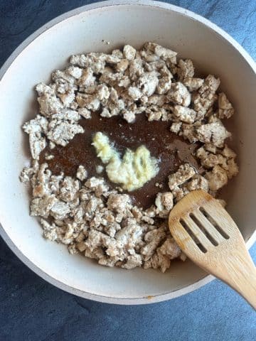 A pan containing cooked ground chicken, soy sauce, and minced ginger inside.