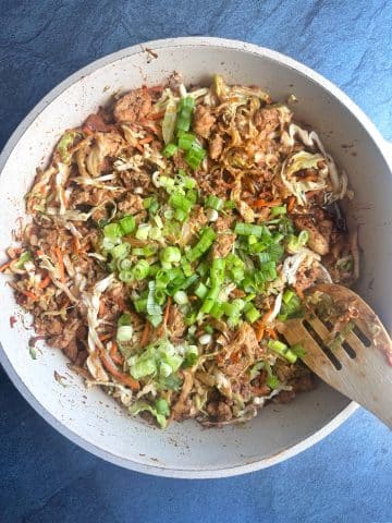 A white pan containing cooked Egg Roll filling with chopped green onions on top.