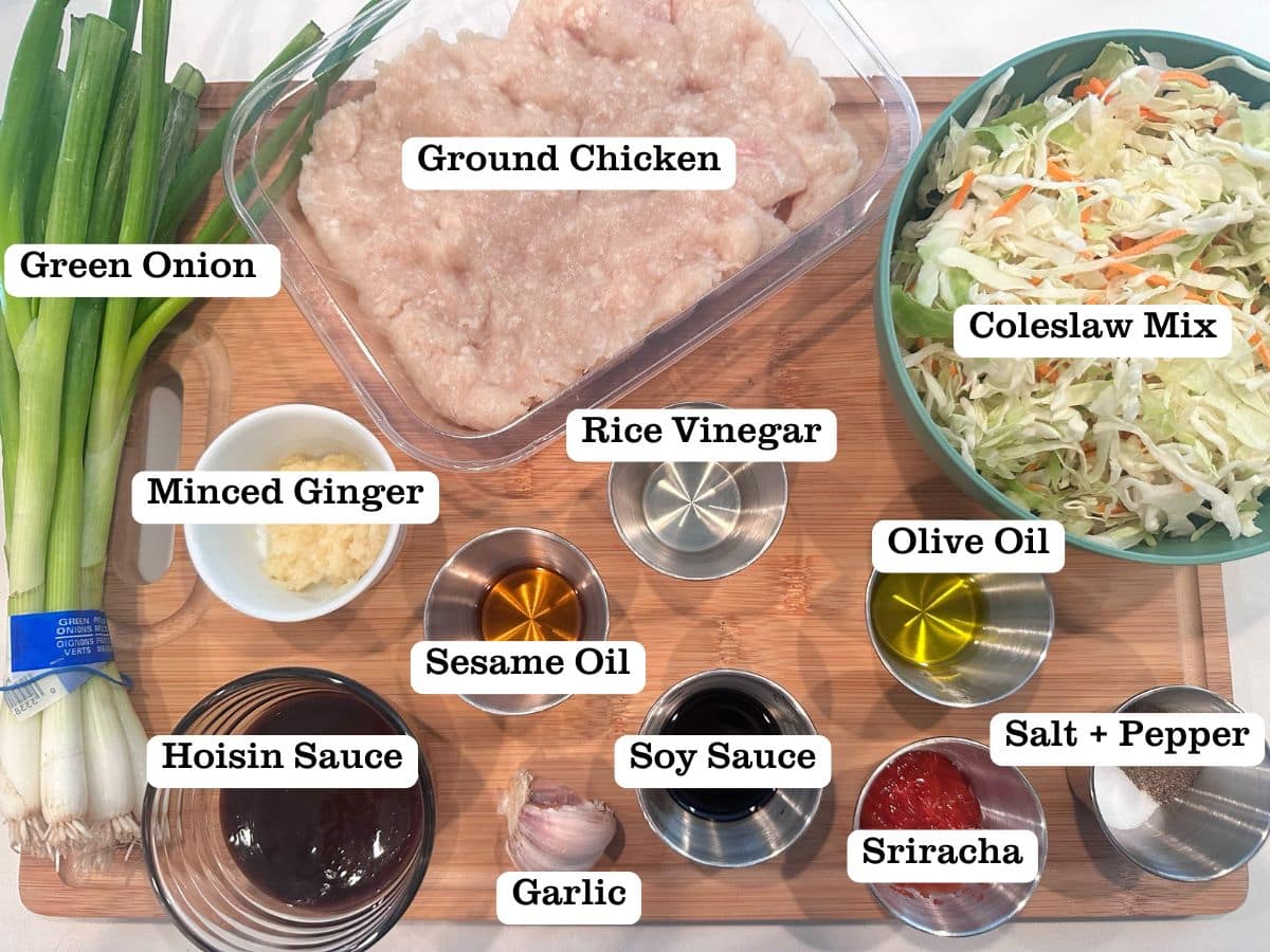 A wooden board containing ingredients for low carb Egg Roll in a Bowl, including ground chicken, coleslaw mix, and hoisin sauce.