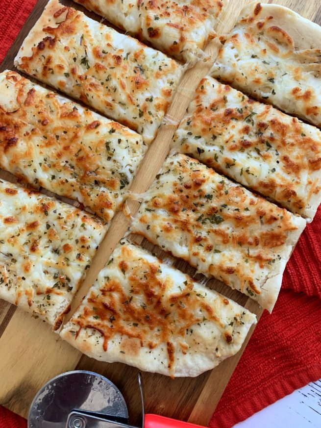 air fried cheesy garlic breadsticks on wooden board with pizza cutter
