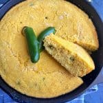 A cast iron skillet containing jalapeño cornbread, with a slice cut out and turned askew.