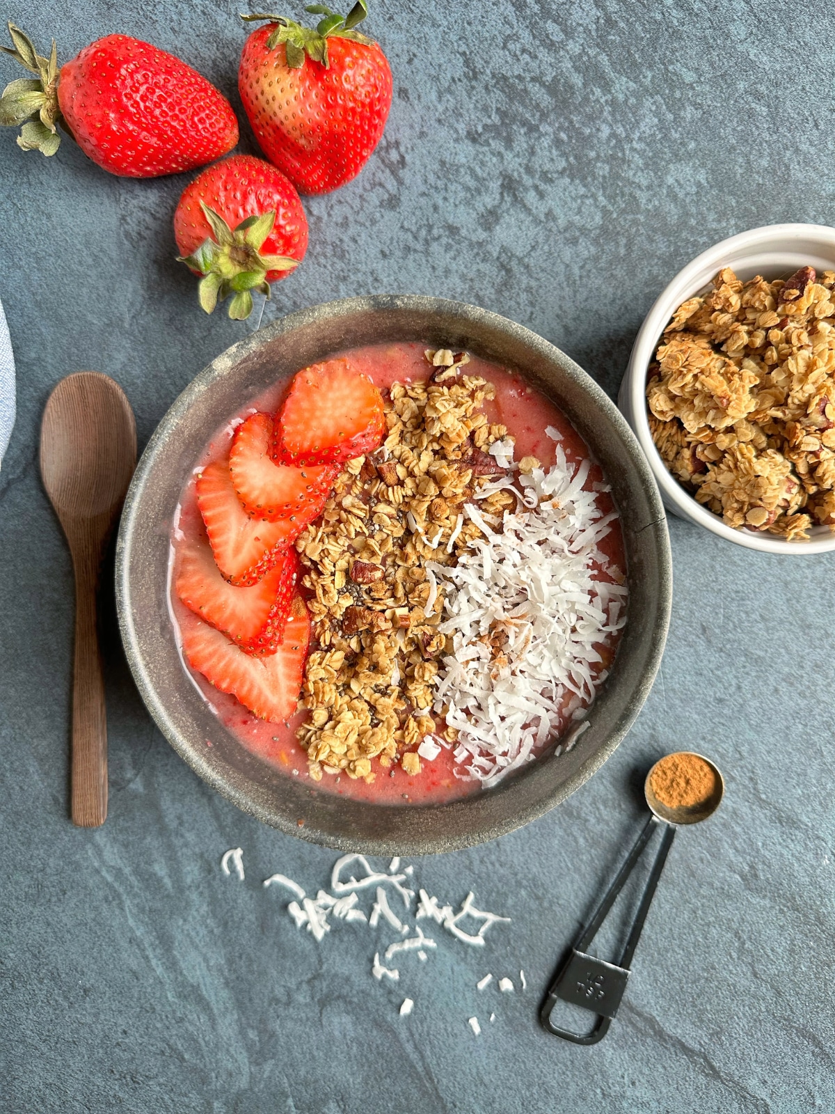 A bowl filled with a pink smoothie with containers of the ingredients and toppings next to it.