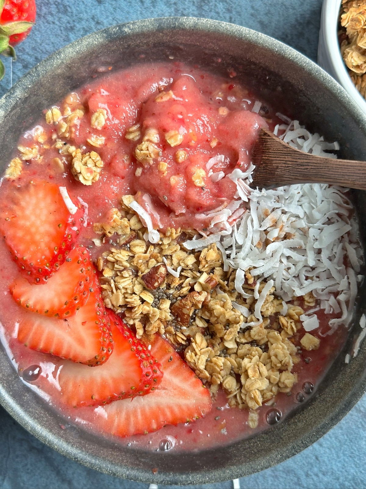 A spoon scooping up a bite of a strawberry smoothie bowl.