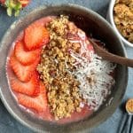 A strawberry mango smoothie bowl with berries, granola, and coconut on top.