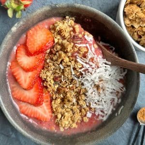 A strawberry mango smoothie bowl with berries, granola, and coconut on top.