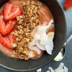 A strawberry-mango smoothie bowl with coconut flakes and granola on top.