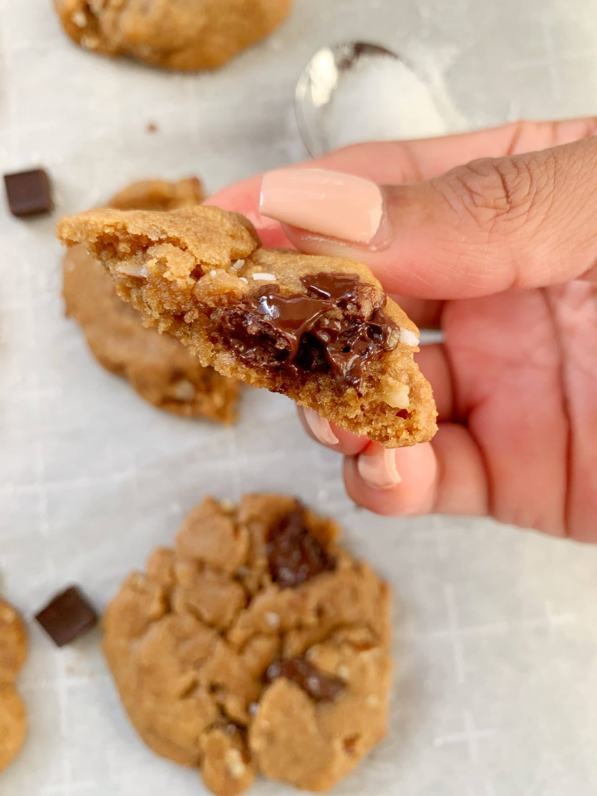 A brown hand holding a brown butter chocolate chip cookie.