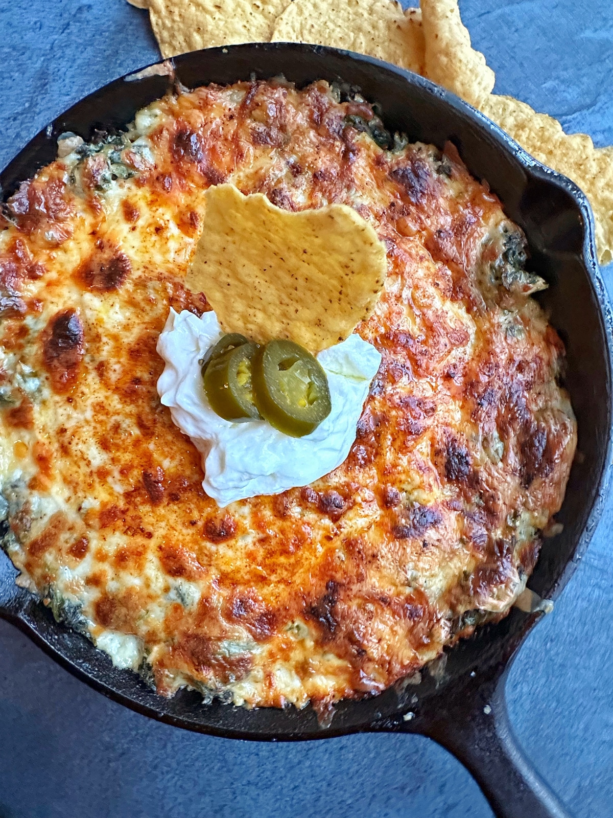 Creamy Hot Spinach Dip in a cast iron skillet, with sour cream and jalapeños on top.