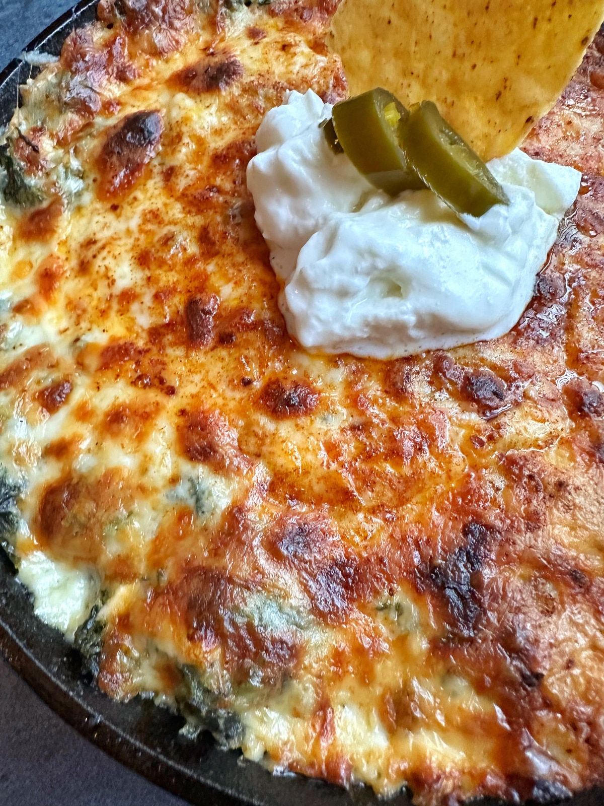 A closeup shot of Creamy Hot Spinach Dip with sour cream and jalapeño pieces on top.