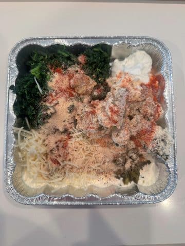 An aluminum pan filled with the ingredients for a spinach dip, to be baked.