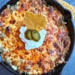 A cast-iron skillet filled with creamy hot spinach dip, with sour cream and jalapeños on top.
