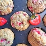 A muffin pan filled with bakery-style strawberry muffins with sliced berries placed around the muffins.