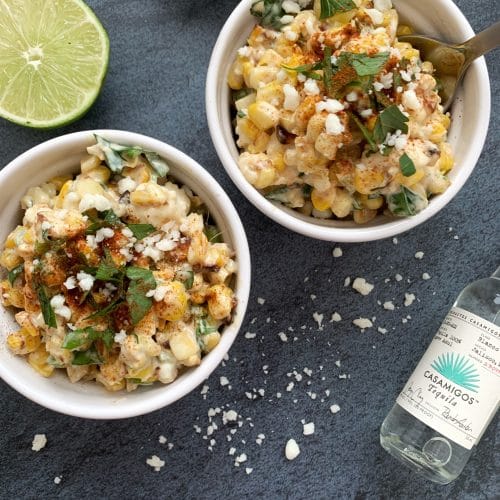 two bowls of mexican corn salad (esquites) with tequila and a lime on the side