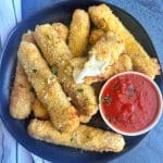 A black plate of air fryer mozzarella sticks with a cup of marinara sauce.