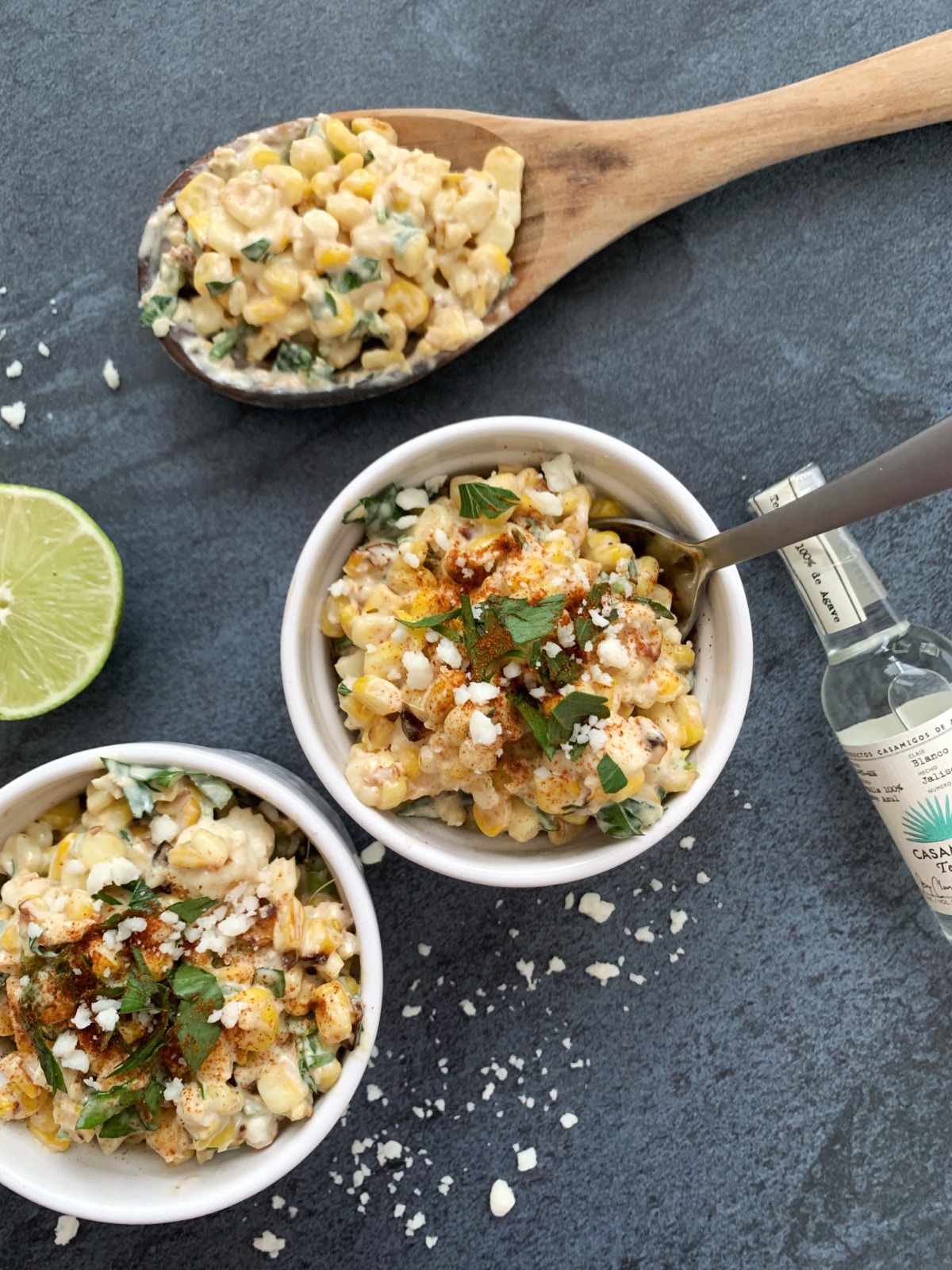 Two bowls of Mexican street corn salad (esquites) on a blue background.