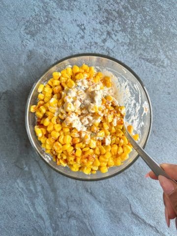 A hand stirring charred corn into a spiced cream mixture.