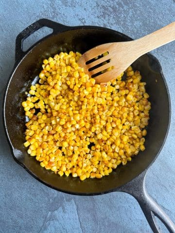 A cast iron skillet filled with charred corn and a wooden spoon.