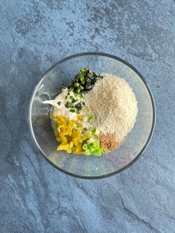 A mixing bowl filled with cotija cheese, chopped cilantro, chopped jalapeno, chopped green onion, and mayonnaise.