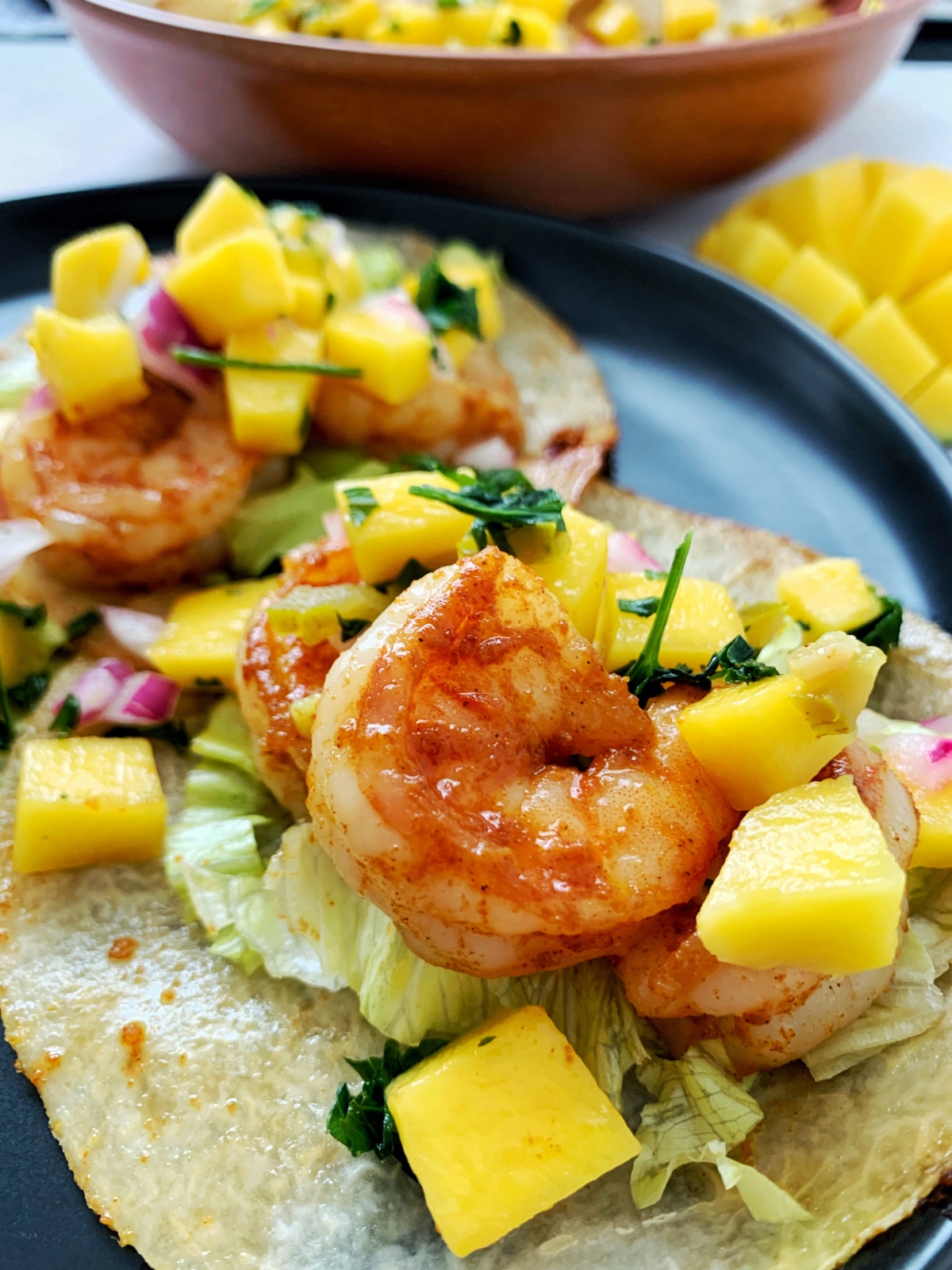A closeup shot of two shrimp jicama tacos on a black plate.