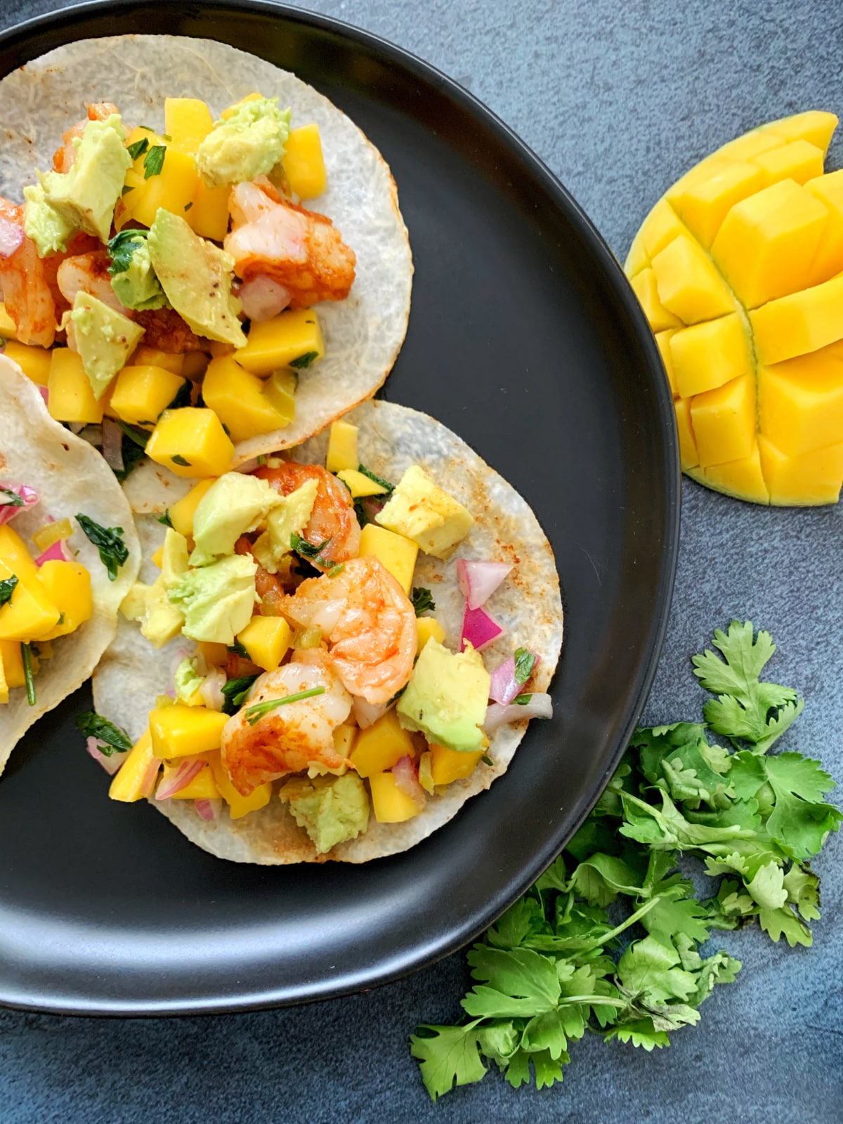 A black plate containing shrimp tacos on jicama wraps with mango salsa on top.
