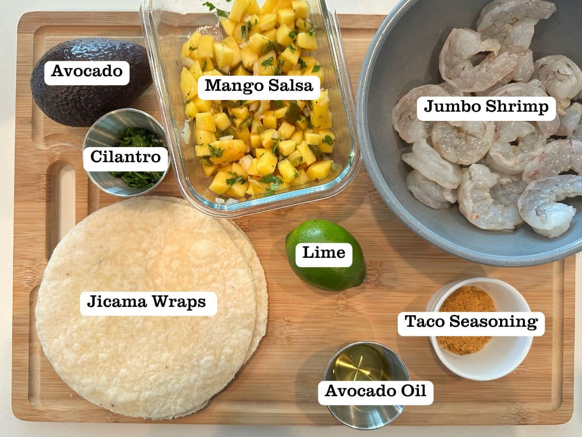 A wooden board containing bowls of ingredients for shrimp tacos on jicama tortillas.