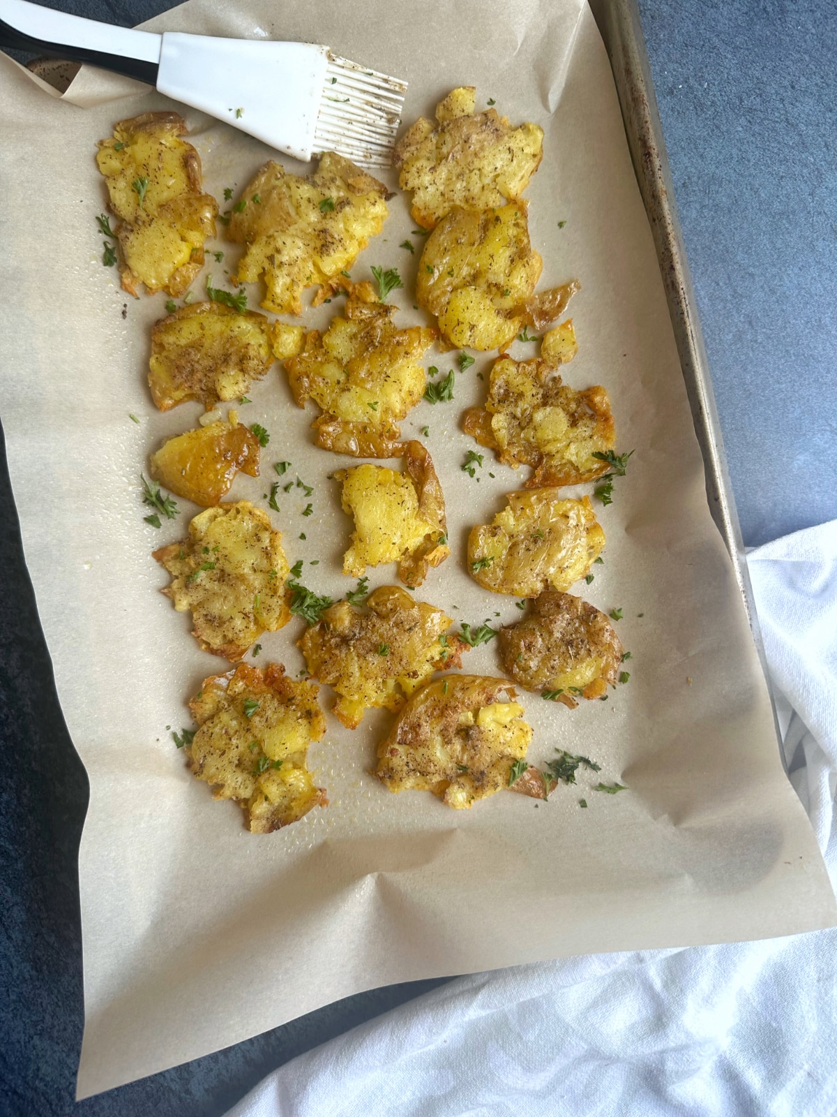 A sheet pan covered in parchment paper with a serving of smashed potatoes and a pastry brush on it.