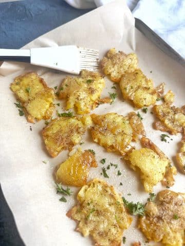 A pan covered with parchment paper and crispy smashed potatoes.
