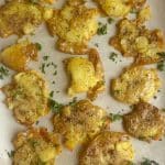 A pan of seasoned Crispy Smashed Potatoes on parchment paper.