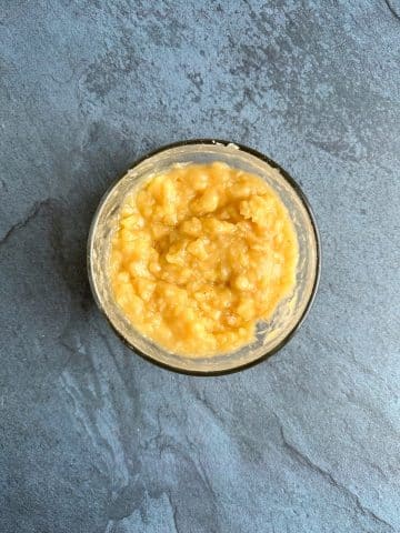 A glass mixing bowl filled with mashed bananas.