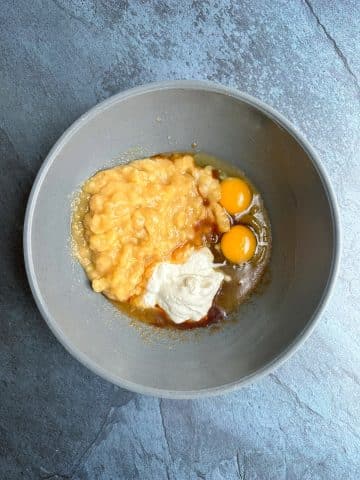 A mixing bowl containing mashed bananas, eggs, greek yogurt, and browned butter base.