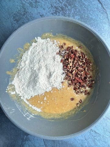 A mixing bowl containing banana bread batter, with flour and nuts on top.