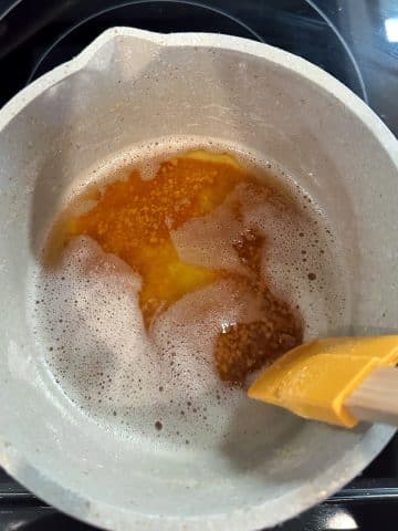 A saucepot filled with browned butter and a silicone spatula dragging in between the foam on top.