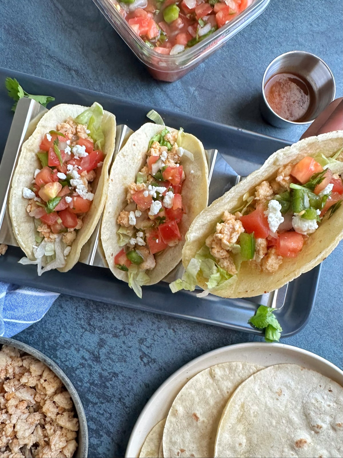A hand picking up a ground chicken taco for display, with more in the background.