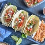A plate of three ground chicken tacos in a taco stand with Mexican rice on the side.