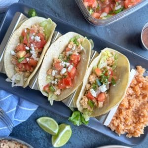 A plate of three ground chicken tacos in a taco stand with Mexican rice on the side.
