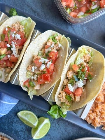 A plate of three ground chicken tacos in a taco stand with Mexican rice on the side.