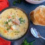 A bowl of non dairy chicken pot pie soup with a stack of biscuits on the side and fresh parsley.