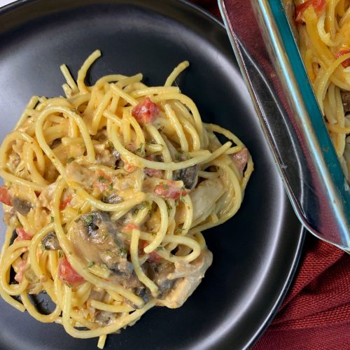 Creamy chicken tetrazzini with mushrooms, tomatoes, and cream sauce on a black plate.