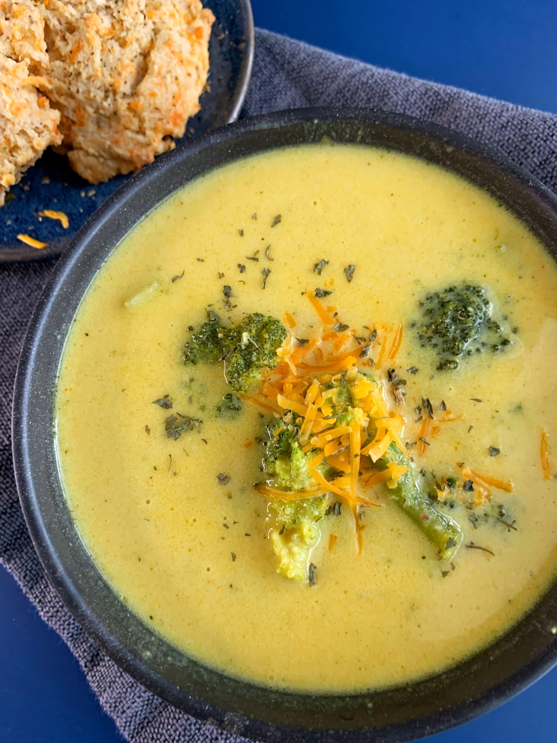 a bowl of broccoli cheddar soup with cheddar bay biscuits on the side