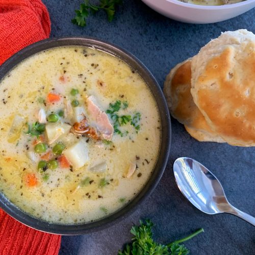 A bowl of non dairy chicken pot pie soup with a stack of biscuits on the side and fresh parsley.