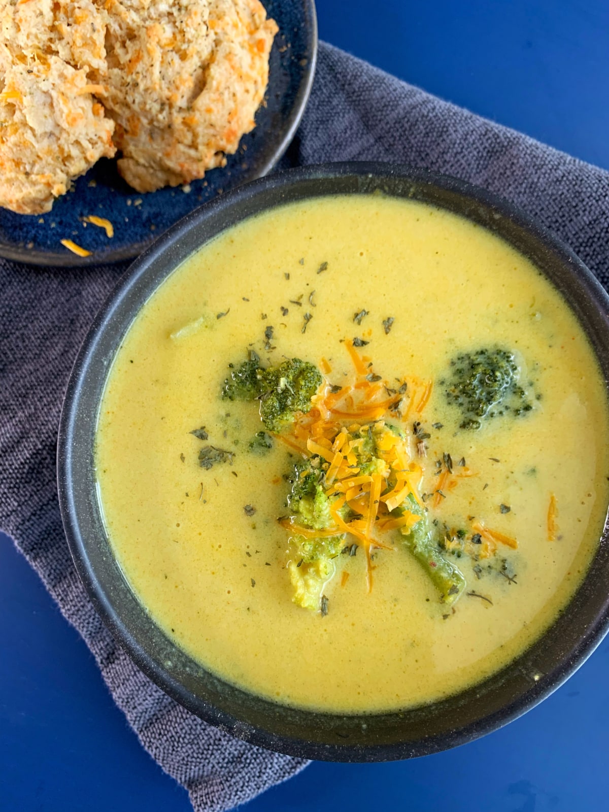 A bowl of broccoli cheddar soup with cheddar drop biscuits on the side.
