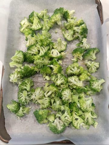 A sheet pan of chopped broccoli and oil, before roasting.