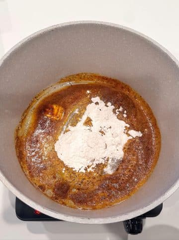 A dutch oven with melted butter, seasonings, and flour inside.