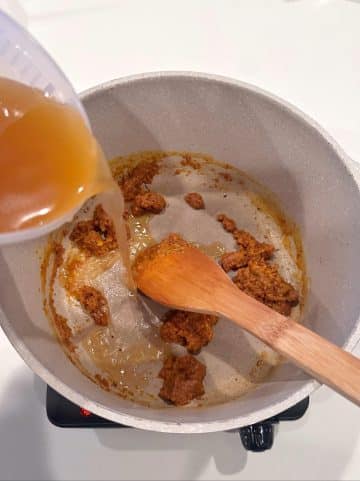 Vegetable stock being poured into a dutch oven with a seasoned roux.
