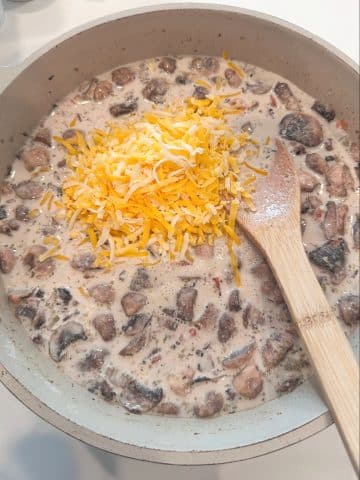 A pan filled with cream sauce, mushrooms, and shredded cheese.